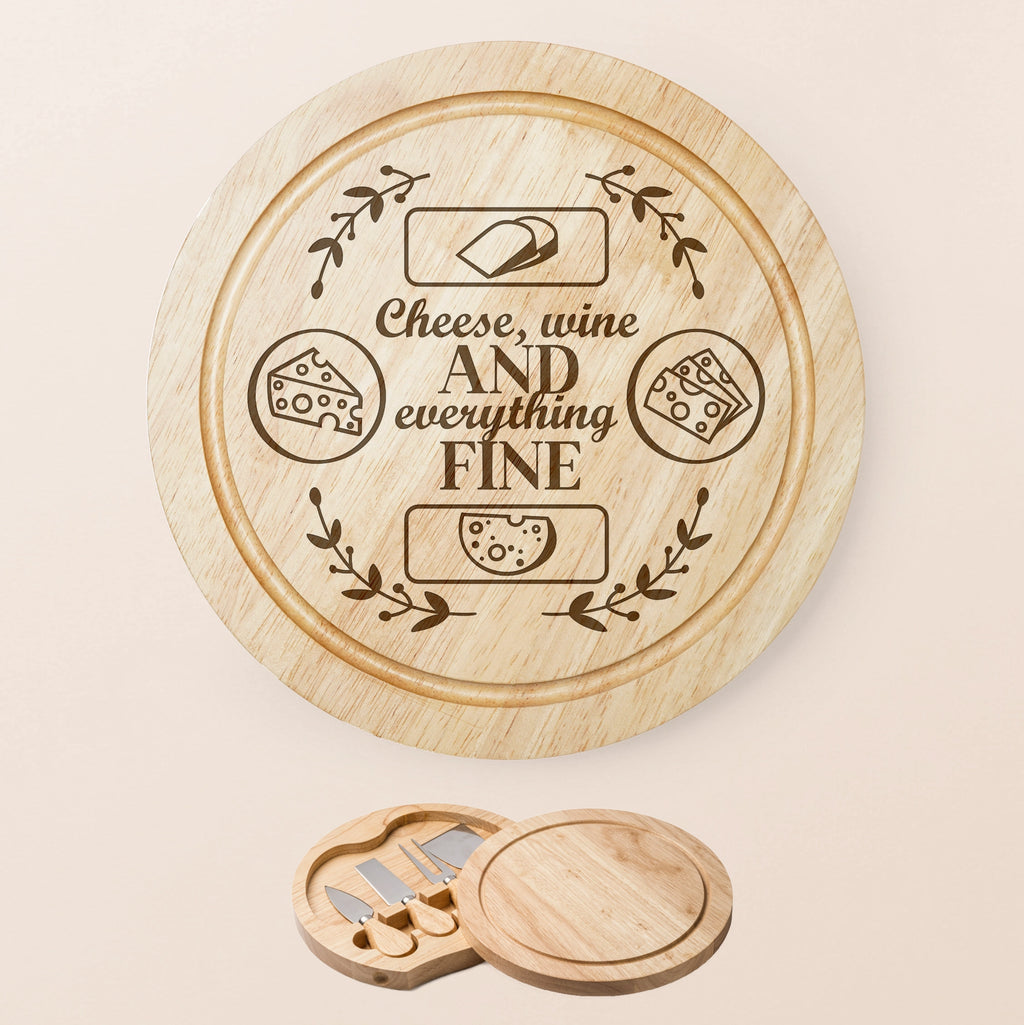A round wooden cheese board set with engraved text reading 'Cheese, wine AND everything FINE' and cheese illustrations, shown on a light beige background. A smaller inset at the bottom shows the matching wooden cheese knives and board lid.