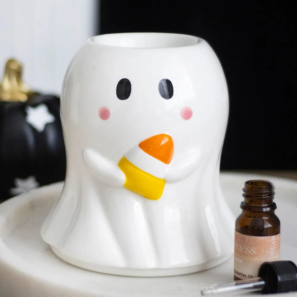 A ceramic oil burner shaped like a ghost holding a candy corn