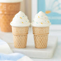 Two ice cream cone-shaped shakers with white cream on a marble surface.