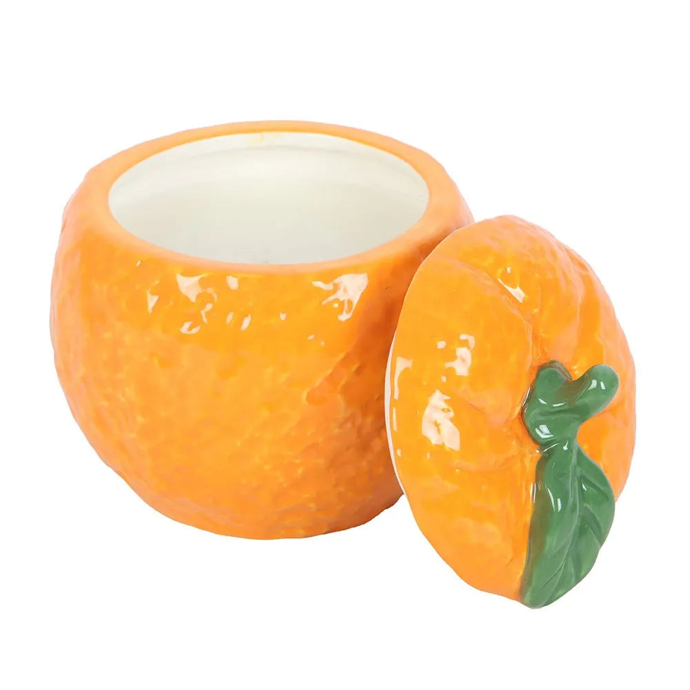 Ceramic candle in a container shaped like an orange with a green leaf lid on a white background