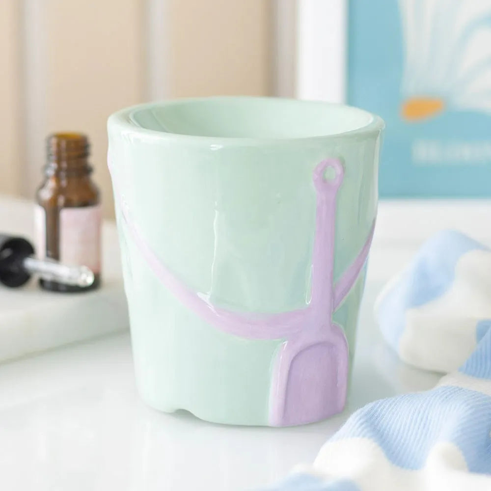 Light green bucket oil burner with pink handle on a blurred background