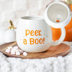 a round white mug printed with 'peek a boo' with a 3D ghost inside.