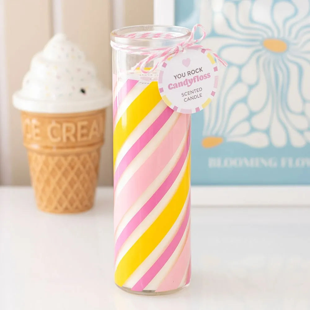 candyfloss scented candle with yellow and pink design on a white surface, with an ice cream cone and book in the background.