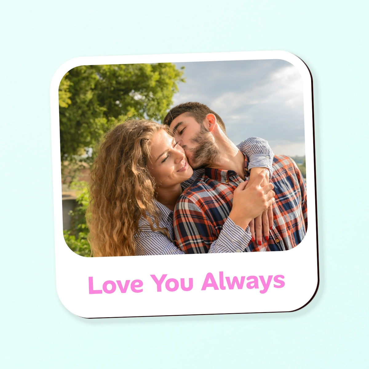 A square photo upload coaster with rounded corners, featuring a picture and chosen text message, shown on a pale mint background.