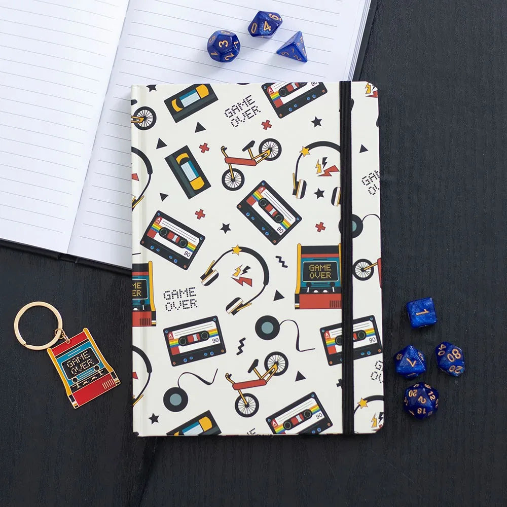 Notebook with retro-themed cover featuring cassette tapes, headphones, and video games on a black surface.