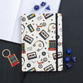Notebook with retro-themed cover featuring cassette tapes, headphones, and video games on a black surface.