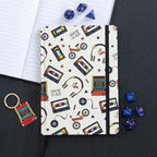 Notebook with retro-themed cover featuring cassette tapes, headphones, and video games on a black surface.