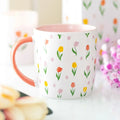 White mug with floral pattern and pink handle on a blurred background
