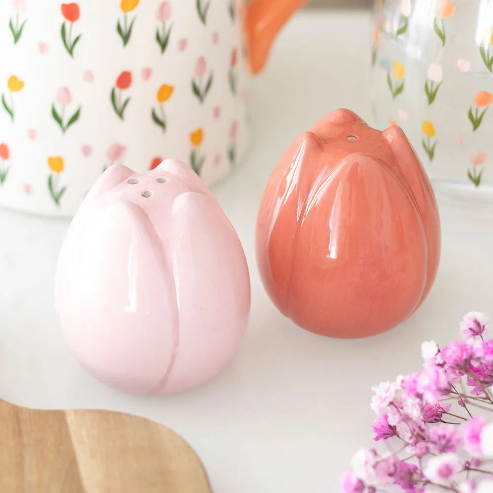 Two tulip-shaped salt and pepper shakers on a white surface with floral-patterned background.