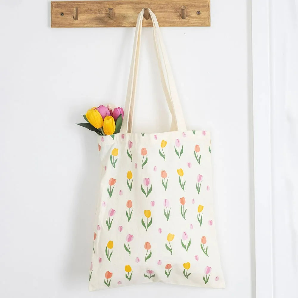 Tote bag with tulip pattern and flowers hanging on a wooden hook.