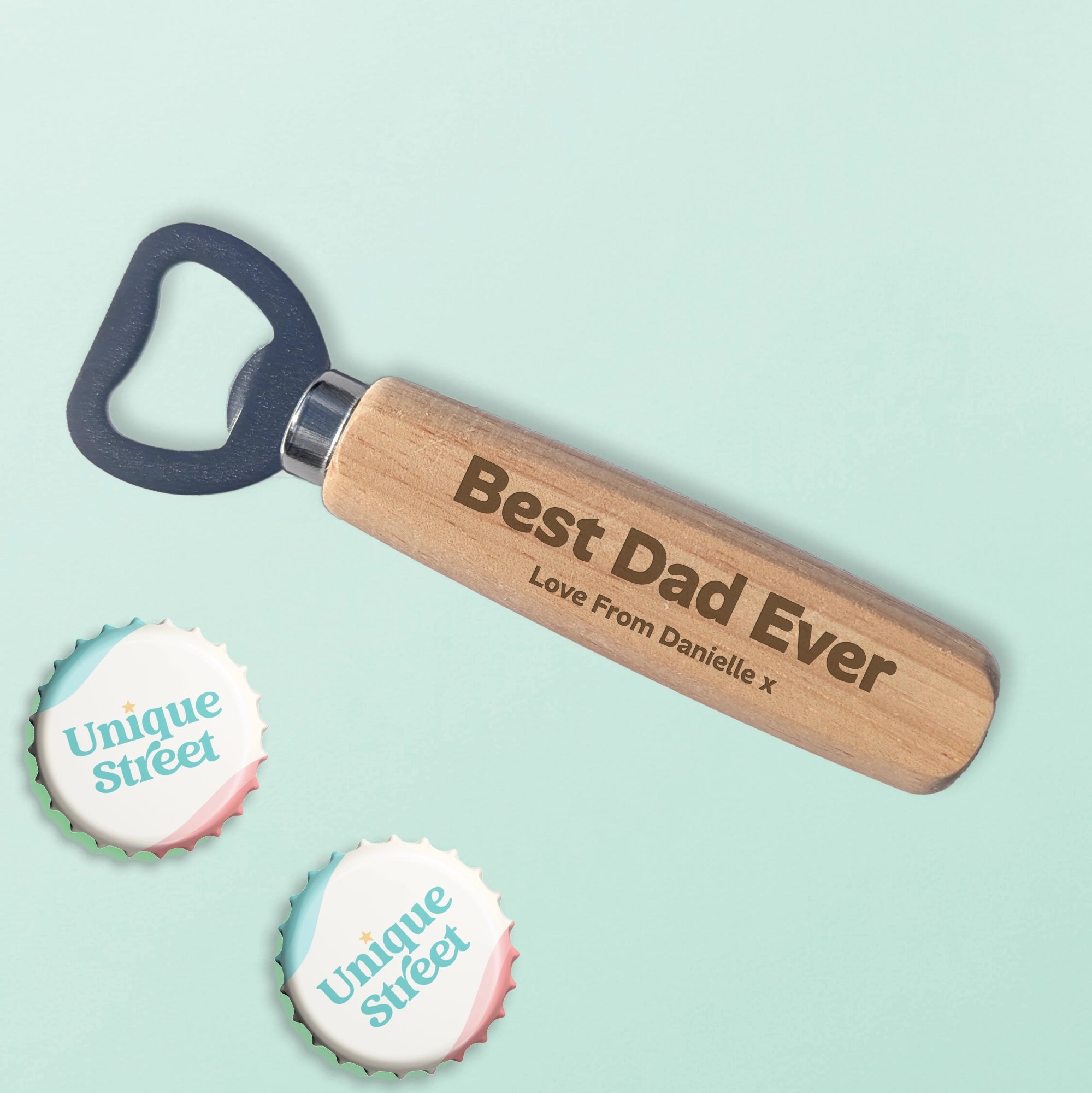 A personalised wooden bottle opener, engraved with 'Best Dad Ever' and message, shown on a light mint green background with two decorative bottle cap labelled 'Unique Street'.