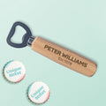A personalised wooden bottle opener with engraved text reading 'name and  Est. year', shown on a light mint green background with two decorative bottle caps labelled 'Unique Street' in the lower left.