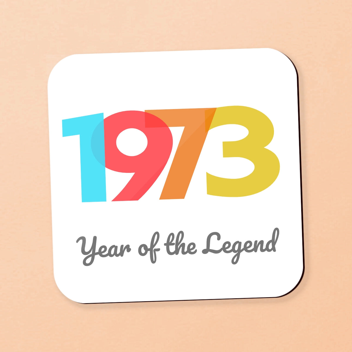 A square white coaster with rounded corners, featuring the colorful numbers '1973' and the phrase 'Year of the Legend' in gray script, set against a solid peach background. personalise with your year